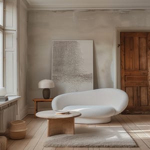 May include: A living room with a white, curved sofa, a round wooden coffee table, and a beige rug. A textured artwork hangs on the wall, with a table lamp and a woven basket. The room has a neutral colour palette, with wooden flooring and a wooden door.