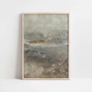 May include: Abstract art print in a light wooden frame. The artwork features a textured, layered design with a color palette of muted blues, browns, and grays. The piece evokes a sense of landscape or atmospheric depth.