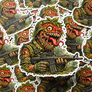 May include: A collection of stickers featuring a grotesque soldier with a strawberry-like head, holding a rifle. The soldier's face is a mix of red, green, and yellow, with a long, protruding tongue. The stickers have a white border.
