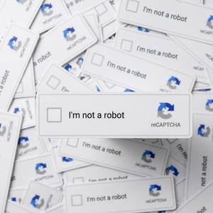 May include: A collection of white rectangular reCAPTCHA verification boxes, each with the text "I'm not a robot" and a checkbox. The reCAPTCHA logo, featuring a blue and gray arrow, is visible on each box. The boxes are scattered across a white surface.