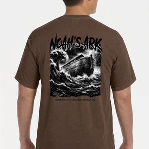 Puede incluir: Camiseta marrón con un gráfico en blanco y negro del Arca de Noé en olas turbulentas. El texto "NOAH'S ARK" está encima de la imagen, con "GENESIS 7:17 | CHOSEN LINEAGE CO." debajo. La camiseta es de color marrón liso.