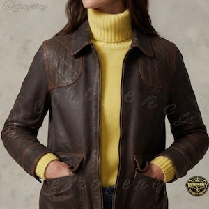 May include: A dark brown leather jacket featuring a front zipper closure, a classic collar, and quilted shoulder patches. The jacket includes two front pockets and is worn over a bright yellow long-sleeve sweater with a high turtleneck collar.