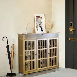 Puede incluir: Un mueble de entrada de madera con tres puertas y detalles de listones verticales. Una obra de arte enmarcada con un estampado de cebra y un bolso blanco encima. Un paraguero con dos paraguas está a la izquierda.