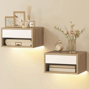 Puede incluir: Dos mesitas de noche flotantes con acabado de vetas de madera y frentes de cajones blancos. Cada mesita tiene un estante abierto y está iluminada con una luz cálida. Una tiene objetos decorativos, la otra un reloj y flores.