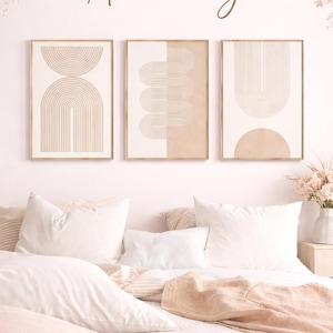 Peut inclure: Trois impressions d'art encadrées avec des motifs géométriques beiges et crème sont accrochées au-dessus d'un lit avec une literie et des oreillers blancs. Le mur est rose clair et le texte "Artevimy" est au-dessus des impressions. Des arrangements floraux décorent le haut du mur.
