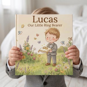May include: A hardcover book titled Lucas Our Little Ring Bearer featuring a cartoon illustration of a young boy in a gray suit holding a gold ring pillow in a field of colorful wildflowers, butterflies, and small birds under a soft sky.