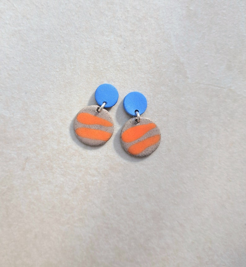 May include: A pair of earrings with orange and gray patterned circles and blue tops.