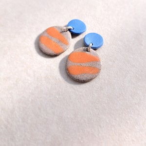 May include: A pair of handmade ceramic earrings with orange and gray striped circles and blue round accents.