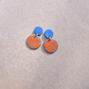 May include: A pair of dangle earrings with orange and gray circular ceramic pieces and blue round tops.