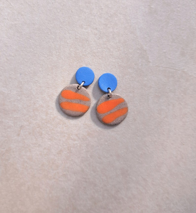 May include: A pair of dangle earrings with orange and gray circular ceramic pieces and blue round tops.