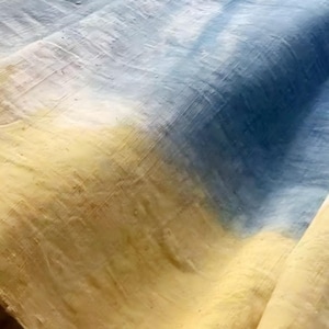 May include: Close-up of a fabric with a colour gradient. The fabric transitions from light yellow to deep blue, with shades of white and gold. The texture appears rough and woven.