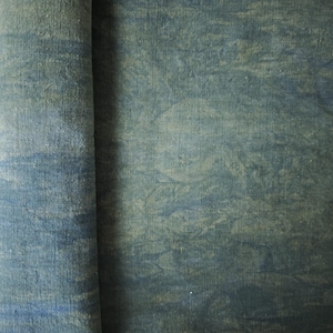 May include: A roll of fabric featuring a mottled, cloud-like pattern in shades of deep blue, slate grey, and muted green. The textile has a visible woven texture with a matte finish, displaying organic, swirling colour variations across the surface.
