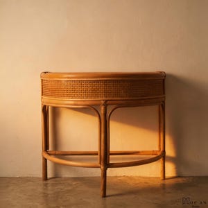 May include: A light brown, half-moon shaped rattan console table. The table has a woven cane front panel and curved legs. The design is a natural, neutral tone, suitable for various interior styles. The table is a decorative furniture piece.