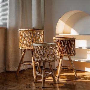 Puede incluir: Tres soportes para plantas de ratán natural de diferentes alturas. Cada soporte presenta un diseño de cesta redonda y tejida con un patrón de diamantes, sostenido por tres patas de madera. Adecuado para plantas de interior, añadiendo un toque bohemio.