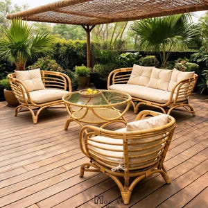 Könnte beinhalten: Gartenmöbel-Set aus Rattan mit einem Zweisitzer-Sofa, zwei Sesseln und einem runden Couchtisch mit Glasplatte. Das Set umfasst beige Kissen und ist auf einer Holzterrasse unter einem gewebten Baldachin angeordnet. Bäume und Grün im Hintergrund.