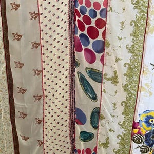 May include: A patchwork textile with diverse patterned fabrics. Designs include repeating brown bird motifs, small pink and black floral patterns, large red and blue polka dots, and green paisley. The fabrics are separated by thin, dark red borders.
