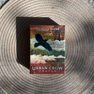 May include: A deck of Urban Crow Oracle cards with a 54-card deck and guidebook. The box features a black crow in flight against a sunset backdrop with the text "MJ Cullinane" and "Urban Crow Oracle".