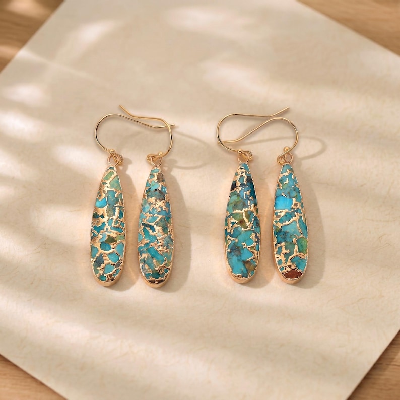 Peut inclure: Deux paires de boucles d'oreilles dor&eacute;es avec des pendentifs en forme de goutte d'eau en turquoise et en pierre dor&eacute;e. Les boucles d'oreilles sont pr&eacute;sent&eacute;es sur une surface claire, mettant en valeur leur design d&eacute;taill&eacute; et le contraste des couleurs.