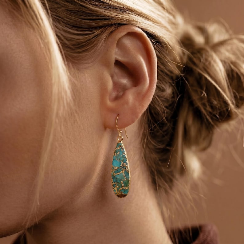 Peut inclure: Boucles d'oreilles pendantes dor&eacute;es en forme de goutte d'eau, incrust&eacute;es d'une pierre turquoise et dor&eacute;e. Les boucles d'oreilles sont suspendues &agrave; un crochet dor&eacute;. Les boucles d'oreilles sont pr&eacute;sent&eacute;es &agrave; c&ocirc;t&eacute; de l'oreille d'une personne.
