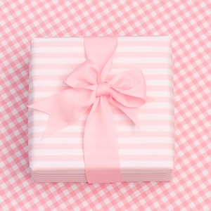 May include: A square gift box wrapped in light pink and white striped paper, featuring a large, centred light pink ribbon bow tied neatly on top. The box has clean, sharp edges and a smooth finish, presenting a classic and uniform appearance.