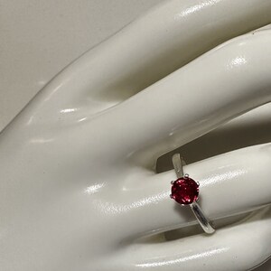 May include: A silver ring with a red gemstone set in a prong setting.