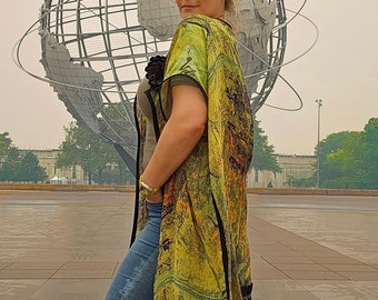 May include: A woman wearing a green and black patterned kimono with a black trim, standing in front of a large globe sculpture. She is wearing blue jeans and has her hand in her pocket.