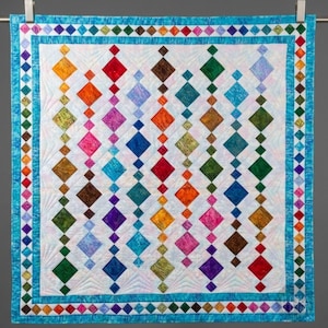 May include: A colorful quilt with a white background and rows of diamond shapes in various colors, including red, orange, green, and blue. The quilt has a blue border with diamond patterns and is hung on a clothesline.