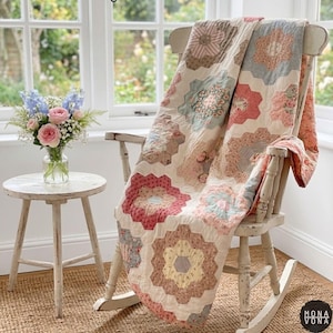 May include: A handmade quilt draped over a white rocking chair. The quilt features a floral pattern in shades of pink, red, blue, and beige. A small side table holds a vase of flowers. The overall aesthetic is vintage and cozy.
