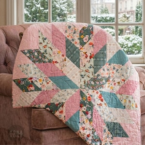 Puede incluir: Un edredón hecho a mano con un diseño de estrella, con telas rosas, turquesas y estampadas con flores. El edredón está sobre un sillón rosa, con una escena nevada visible a través de una ventana en el fondo.