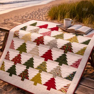 May include: A handmade Christmas tree quilt with a white background and red border. The quilt features rows of colorful Christmas trees in various patterns and colors, including red, green, and gold. A cup of coffee and a book rest on a wooden table.