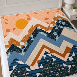 May include: A geometric mountain range quilt in shades of blue, orange, and white. The quilt features a sun design and a forest scene at the bottom. The quilt is on a white bed.