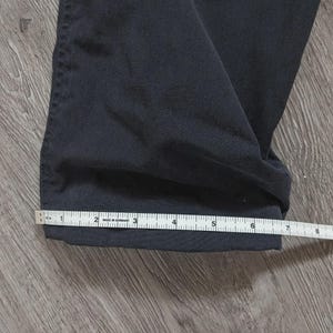 May include: A pair of dark navy blue trousers with a straight hem. A white measuring tape is positioned across the bottom of the pant leg, showing a width measurement of approximately 25.4 cm from the folded edge to the side seam.
