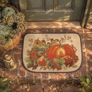 May include: A rectangular doormat with rounded corners featuring a woven tapestry design of a large orange pumpkin, red apples, green leaves, and small berries. The mat has a dark brown border and a light beige background with a textured finish.