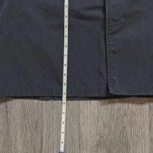 May include: A dark navy blue garment featuring a straight hemline and a vertical seam. A white measuring tape is positioned vertically against the fabric, showing a length measurement extending from approximately 81 cm down to 117 cm.