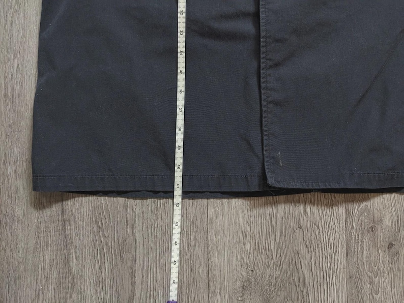 May include: A dark navy blue garment featuring a straight hemline and a vertical seam. A white measuring tape is positioned vertically against the fabric, showing a length measurement extending from approximately 81 cm down to 117 cm.