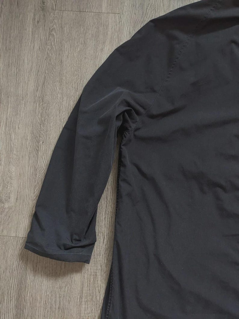 May include: A solid black long-sleeve shirt featuring a smooth, matte fabric texture. The garment has a simple, clean design with a standard sleeve construction and a straight hemline, showcasing a plain and uniform dark colour throughout the piece.