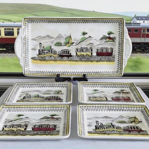 May include: A set of vintage train-themed serving dishes. The set includes a large rectangular tray with handles and four smaller rectangular plates. Each piece features a train scene with a yellow border and a decorative edge.