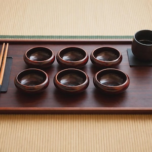 May include: A white ceramic mug with a black handle and the text "But First, Coffee" in a black, bold font. The mug is sitting on a wooden surface. The mug is approximately 4 inches tall.