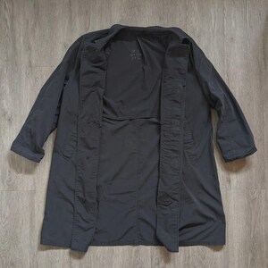 May include: A dark charcoal grey trench coat featuring a wide collar, long sleeves, and a front button closure. The interior lining displays the text "BEN DITO US" printed in a subtle font. The coat has a structured silhouette with visible seams.