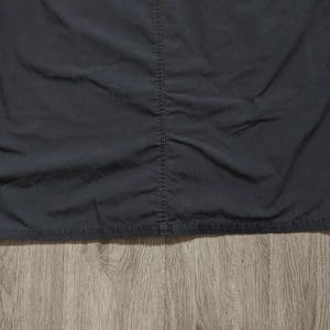 May include: A solid black shirt featuring a prominent vertical seam running down the centre. The fabric has a matte finish with visible stitching along the hem and the central seam, creating a structured appearance across the front of the garment.