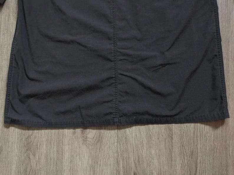 May include: A solid black shirt featuring a prominent vertical seam running down the centre. The fabric has a matte finish with visible stitching along the hem and the central seam, creating a structured appearance across the front of the garment.