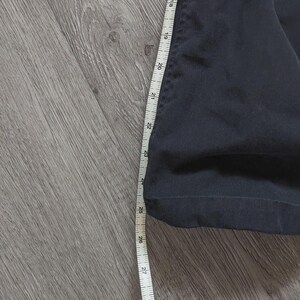 May include: A dark navy blue garment leg section featuring a straight hem, positioned alongside a white measuring tape that indicates a length measurement extending from approximately 43 cm to 74 cm along the side of the fabric.