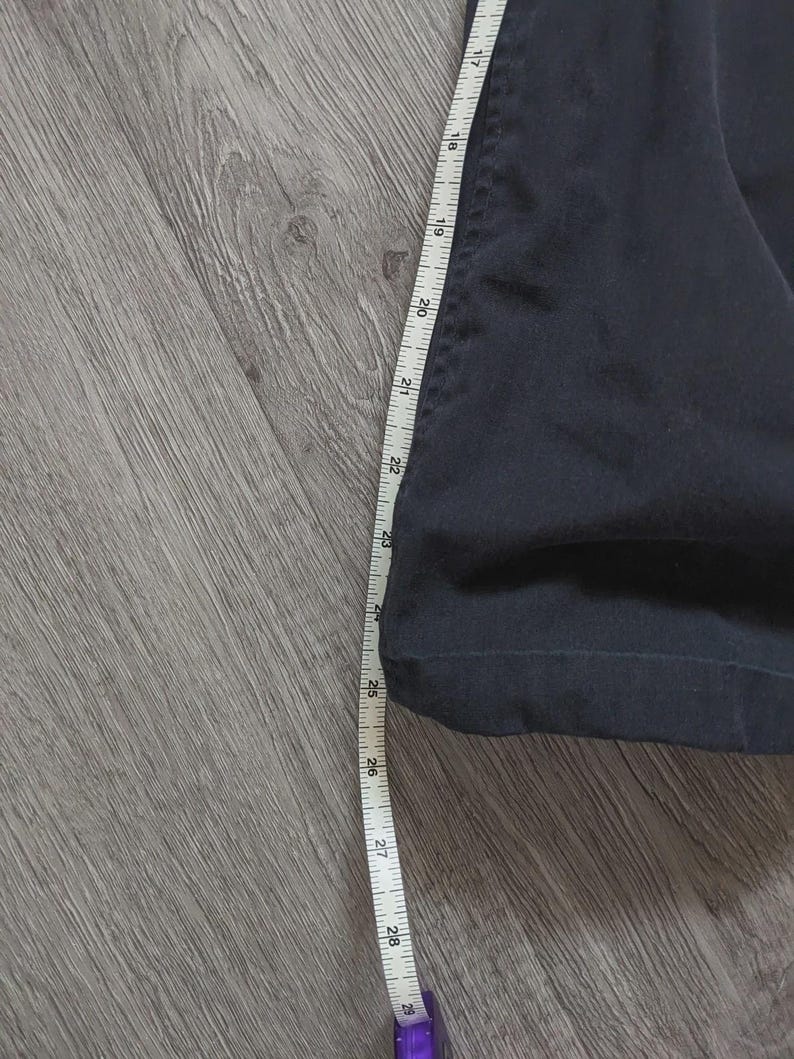 May include: A dark navy blue garment leg section featuring a straight hem, positioned alongside a white measuring tape that indicates a length measurement extending from approximately 43 cm to 74 cm along the side of the fabric.