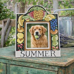 May include: A rectangular picture frame with a white border and a painted fruit motif featuring a pineapple, bananas, grapes, and cherries. The word SUMMER is printed in black capital letters at the bottom. A photo of a golden retriever holding a tennis ball is inside.