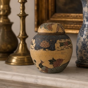 May include: A round ceramic jar with a lid, featuring a yellow base color and a decorative band of dark blue with floral motifs. The body of the jar displays painted illustrations of a peacock and various flowers in shades of red, green, and blue.
