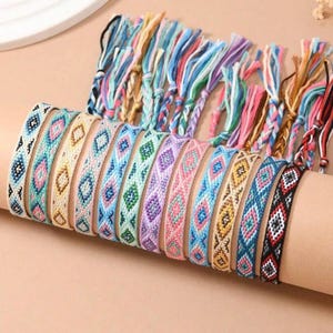 May include: A selection of colourful friendship bracelets with woven geometric patterns. The bracelets feature various colours, including blue, pink, green, and yellow. The image also shows the braided ends of the bracelets.