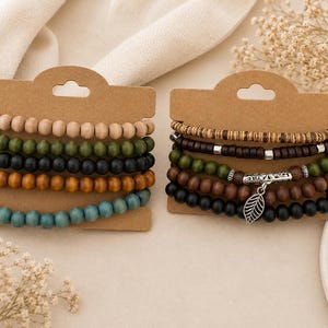 May include: Two sets of wooden bead bracelets on brown cardboard tags. One set has natural, green, black, orange, and blue beads. The other set includes wood, brown, green, and black beads, with a silver leaf charm.
