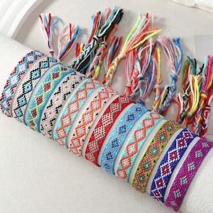 May include: A selection of colourful friendship bracelets with diamond patterns. The bracelets feature various colours including blue, red, orange, green, and purple. Each bracelet is made of woven threads with knotted ends.