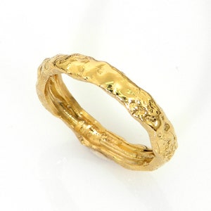Könnte beinhalten: Ein goldener Ring mit einer strukturierten, unregelmäßigen Oberfläche. Der Ring ist dick und hat eine breite Band.