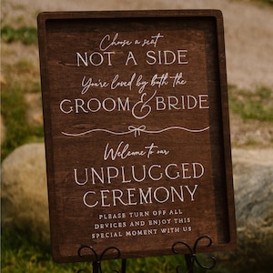 Puede incluir: Un letrero de madera marrón oscuro con texto blanco. El letrero dice: "Elige un asiento, NO UN LADO, Eres amado por el NOVIO y la NOVIA, Bienvenido a nuestra CEREMONIA DESCONECTADA. Apaga todos los dispositivos y disfruta de este momento especial con nosotros."